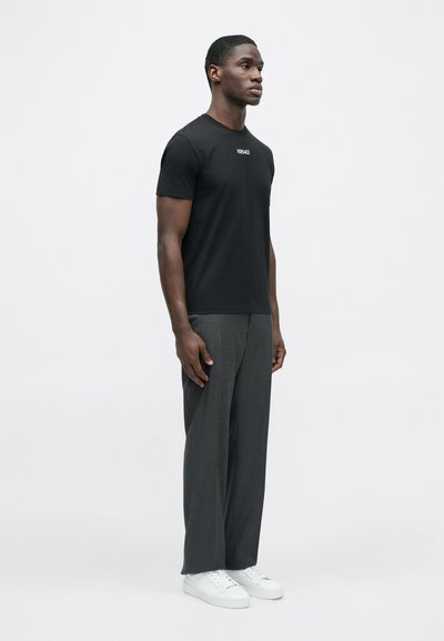 Μαύρο βαμβακερό t-shirt με λαιμόκοψη και διακριτικό λογότυπο, συνδυασμένο με γκρι φαρδιά παντελόνια κ�αι λευκά αθλητικά παπούτσια, εμφανιζόμενο από πλάγια όψη.