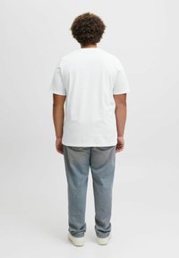 Hvid bomulds-T-shirt med korte ærmer, afslappet pasform og rund halsudskæring, parret med lyseblå denim jeans og hvide sneakers.