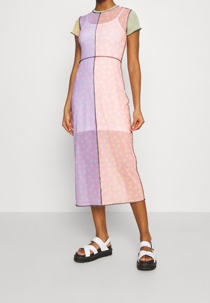 Kvinde iført en pastel patchwork midi kjole med korte ærmer og hvide sandaler med tykke sorte såler.
