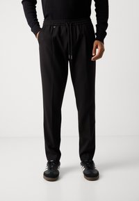 Black sweatpants with adjustable drawstring waist, side pockets, and a relaxed fit. Worn with dark sneakers featuring white stripes.