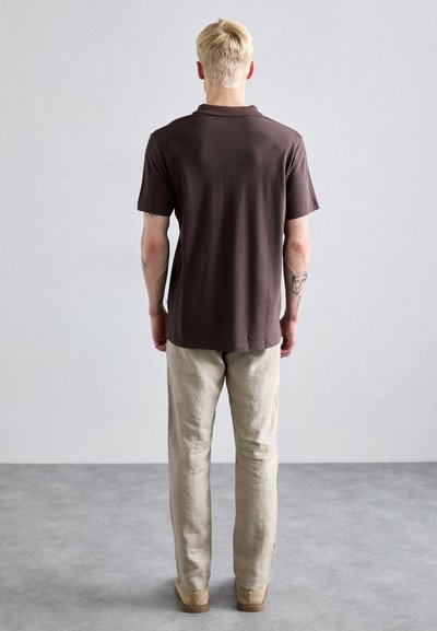 Polo marron, à manches courtes, texture lisse, avec une coupe décontractée. Assorti avec un pantalon en lin beige clair à jambe droite et des chaussures marron.