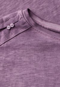 T-shirt en coton violet avec une texture lisse, col rond et deux boutons assortis à l'épaule. Motif texturé vertical subtil.