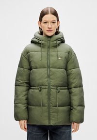 Giacca imbottita verde oliva, con zip frontale, cappuccio regolabile, vita con cordoncino e tessuto testurizzato con dettagli delle cuciture orizzontali.