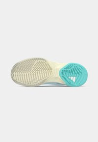 Podplati športnega čevlja z bež podplatom, modrim gumijastim gripom in Adidasovim logotipom pod peto na svetlo sivi podlagi.