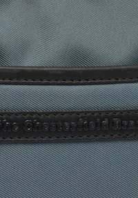 Tessuto blu strutturato con un accentuato in pelle nera liscia. Presenta un marchio impresso sulla pelle e cuciture in contrasto lungo il bordo.