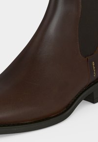 Bottine Chelsea en cuir marron avec empiècement latéral élastique noir et petit talon noir, avec le logo "GANT" sur la languette.