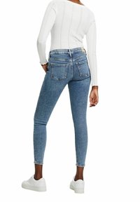 Vaqueros ajustados en denim azul claro con bolsillos traseros y cintura alta, combinados con una camiseta ajustada de manga larga blanca y zapatillas blancas.