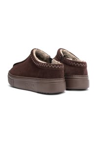 Brązowe zamszowe buty wsuwane z puszystą podszewką, z grubą brązową podeszwą i ozdobnym zygzakowatym przeszyciem wzdłuż górnej krawędzi.