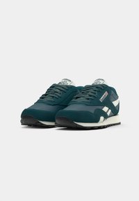 Par tenisica Reebok Classic u tirkiznoj i bijeloj boji s crnim potplatima, prikazanih pod kutem prema naprijed na bijeloj pozadini.