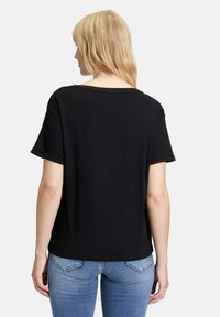 Zwarte korte mouwen T-shirt met een relaxte pasvorm, voorzien van opgerolde mouwen en een ronde halslijn, gecombineerd met lichtblauwe jeans.