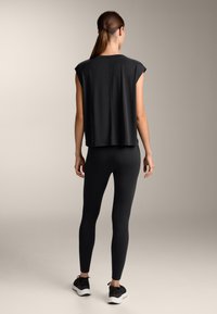 Top atletico nero con maniche a cappuccio, abbinato a leggings neri e scarpe da ginnastica. Tessuto liscio, vestibilità comoda e materiale elastico in tutto.