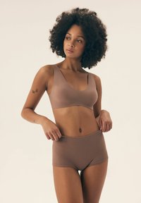 Beżowy bezszwowy biustonosz oraz wysokie szorty w miękkim, bezszwowym materiale. Obydwa elementy wyróżniają się gładką strukturą i minimalistycznym wzornictwem.