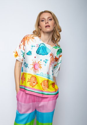 Bunt bedrucktes, kurzärmeliges Oberteil mit aquatischen Motiven auf weißem Hintergrund; darüber eine mehrfarbige gestreifte Hose in Pink und Blau.