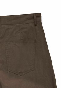 Tissu marron avec une poche arrière cousue et un passant de ceinture sur un pantalon ou un short sur un fond blanc.