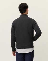 Mørk grå jakke med en glatt tekstur og krage-design. Har knappe-manchetter og en figurvennlig silhuett, lagd over en stripete skjorte.