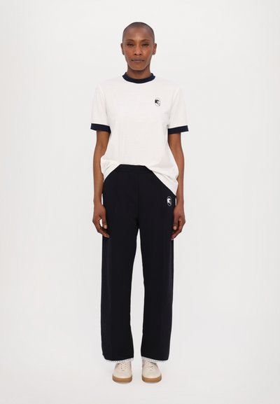 White t-shirt with navy blue ribbed accents, paired with navy wide-leg pants featuring a logo. Light casual shoes with a gum sole.