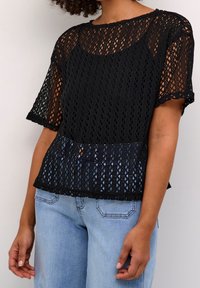 Top nero all'uncinetto con maniche corte, caratterizzato da un intricato motivo a diamante e una vestibilità ampia, abbinato a jeans in denim azzurro chiaro.