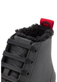 Zwarte leren hoge schoen met een gestructureerd oppervlak, zwarte veters en een harige zwarte kraag, met een rode lus aan de achterkant.