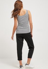 Schwarz-weiß gestreifter Tanktop, kombiniert mit lockeren schwarzen Hosen, die an den Bündchen gerollt sind, und weißen Sneakers mit einem grauen Muster.