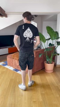 Black t-shirt featuring a white ornate spade design on the back, paired with dark patterned shorts and gray sneakers with white accents.