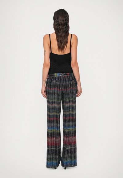 Top nero con spalline e dettagli sul retro, abbinato a pantaloni larghi e plissettati colorati con un motivo a righe metalliche.