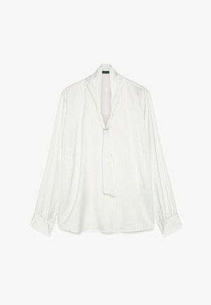 Bílá halenka s dlouhým rukávem, jemnými vertikálními pruhy, hlubokým výstřihem do V a malou ozdobnou sponou na předním límci.