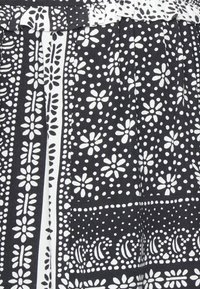 Černá látka s bílými květinovými a geometrickými vzory, vybavená sklady a designem řaseného pasu. Měkká textura a kontrastní barvy.