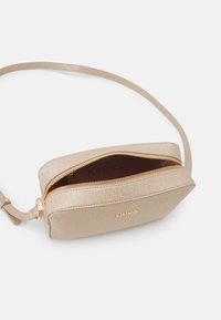 Borsa a tracolla beige con finitura texturizzata, zip dorata e dettaglio del logo. La parte superiore aperta mostra un interno a contrasto. Include una tracolla regolabile.