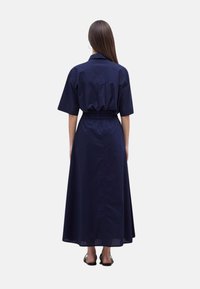 Vestido largo azul marino con mangas cortas, con un cinturón elástico y un detalle de yugo en la parte posterior. Hecho de tela liviana.
