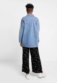 Světle modrá džínová bunda s volným střihem, dlouhými rukávy, bočními kapsami a zadním průkrčníkem, doplněná černými kalhotami s puntíky.