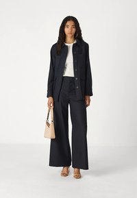 Morski garnitur w prążki z marynarką na guziki i szerokimi spodniami. Modelka trzyma małą beżową torebkę i nosi sandały na paski.