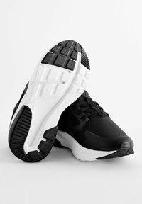 Des chaussures de sport noires au design épuré, avec des tiges en mesh et une semelle intercalaire blanche rembourrée dotée d'un motif de grip texturé et de lacets.