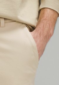 Beige bikses, izgatavotas no gludas auduma, ar sānu kabatu. Jostasvietai ir smalka šuvuma detaļa un tīrs, pielāgots izskats.