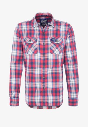 Chemise à carreaux rouge, blanche et bleue à manches longues, boutonnée, avec deux poches poitrine et une petite étiquette en tissu sur la poche gauche.