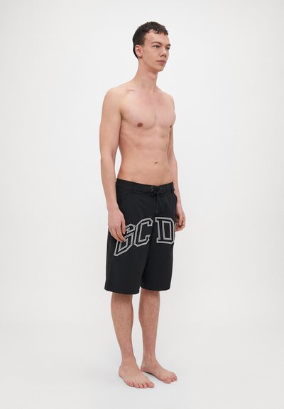 Černé plavkové šortky s bílým nápisem "GCD". Mají stahovací pás, boční kapsy a délku ke kolenům. Hladká, lehká tkanina.