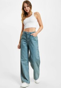 Bílý proužkovaný crop top v kombinaci s světle modrými širokými džíny, které mají vysoký pas a jemné vyblednutí. Nosí se s bílými teniskami.