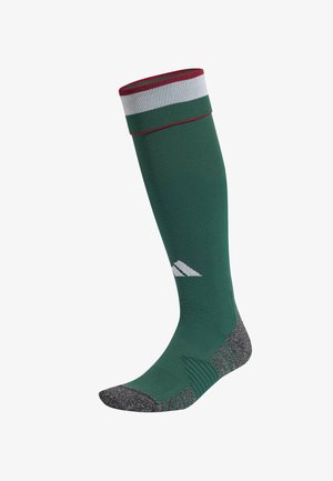 Calcetín verde hasta la rodilla con parte superior a rayas rojas y blancas. Cuenta con una plantilla texturizada gris con secciones de soporte acanaladas y un logo.