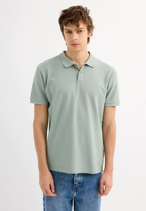 Polo de color verde claro hecho de algodón, con cuello y mangas cortas. Cuenta con un logo sutil en el pecho y una textura suave.