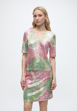 Vrouw draagt een pailletten top met korte mouwen en V-hals en een bijpassende rok met een meerkleurig abstract bloemmotief.