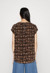 Svart blus med kort ärm och detaljerade geometriska mönster i orange och krämfärg, rundad nederkant och dragkedja bak.