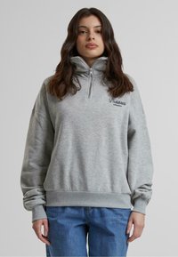 Sudadera de cremallera gris claro con cuello alto, puños y dobladillo acanalados. Presenta el texto "Prendas Prohibidas" en negro. Textura suave.