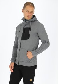 Grijze rits hoodie met een zwart borstzakje, verstelbare capuchon en voorzakken; gemaakt van textuurstof met een getailleerd ontwerp.