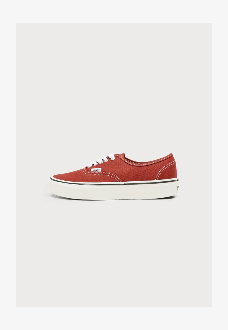 Baskets basses en toile rouge rouille avec lacets blancs, semelle en caoutchouc blanche et logo Vans sur le côté et le talon, vues de côté.