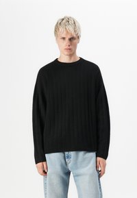Sort ribbet sweater med rund hals og dropped shoulders. Blød tekstur, løs pasform og enkel design. Kombineret med lyseblå jeans.