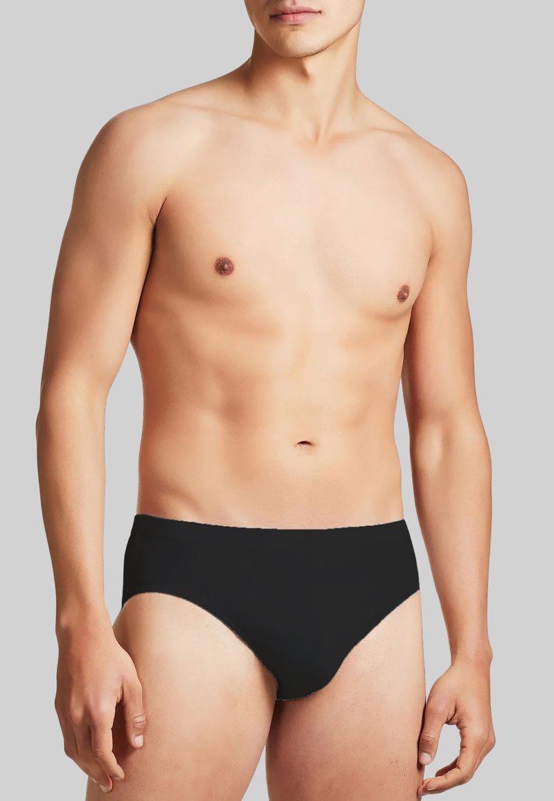 Costume da bagno nero in stile slip, con una texture liscia, vita elastica, design aderente e taglio minimalista, indossato da un modello maschile.