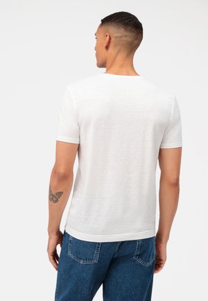 White short-sleeve T-shirt with a round neckline, made of lightweight fabric, featuring a smooth texture and a casual fit, worn with blue jeans.