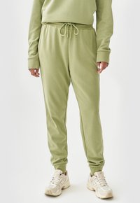 Groene katoen joggers met een elastische tailleband, trekkoord detail en taps toelopende boorden. Draagt met lichtgekleurde sportschoenen.