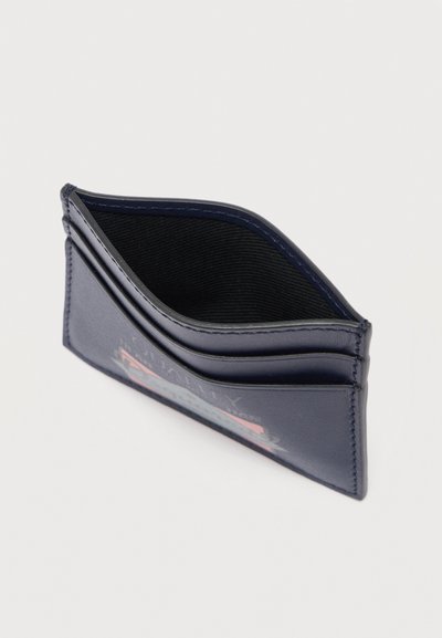 Λεπτή μπλε ναυτική δερμάτινη θήκη καρτών με τρεις θέσεις για κάρτες και τυπωμένο λογότυπο στο μπροστινό μέρος, σε λευκό φόντο.