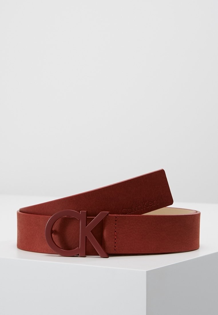 Ceinture en cuir marron enroulée sur une surface blanche avec une boucle marron assortie au logo "CK" et un marquage subtil Calvin Klein sur la lanière.