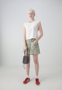 Hvit avkortet topp med gult kantbånd, grønne shorts, røde sneakers og en svart mønstret minibag. Glatte materialer, uformell design.